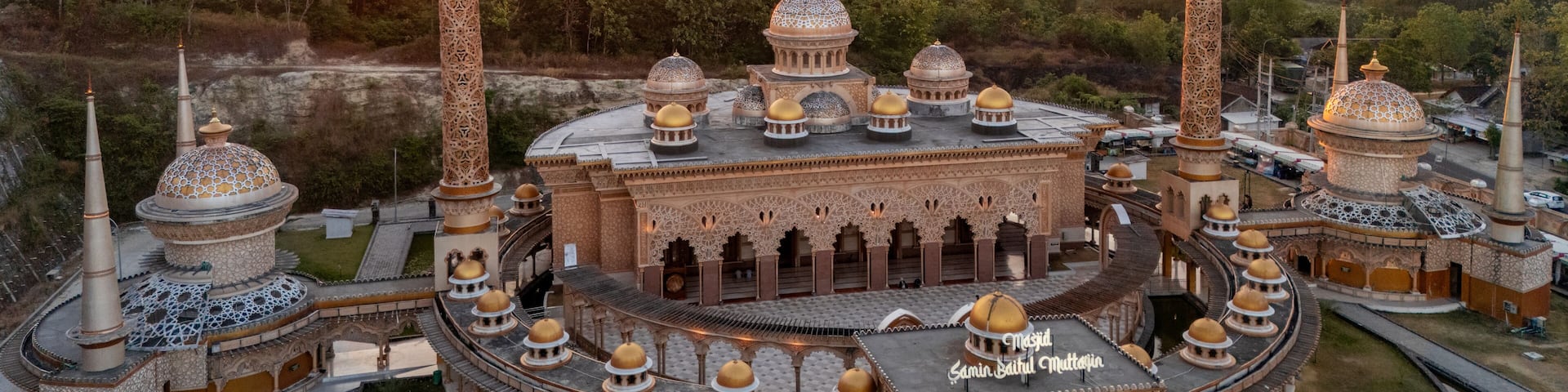 A large, ornate mosque with multiple domes and minarets, surrounded by lush greenery and hills.