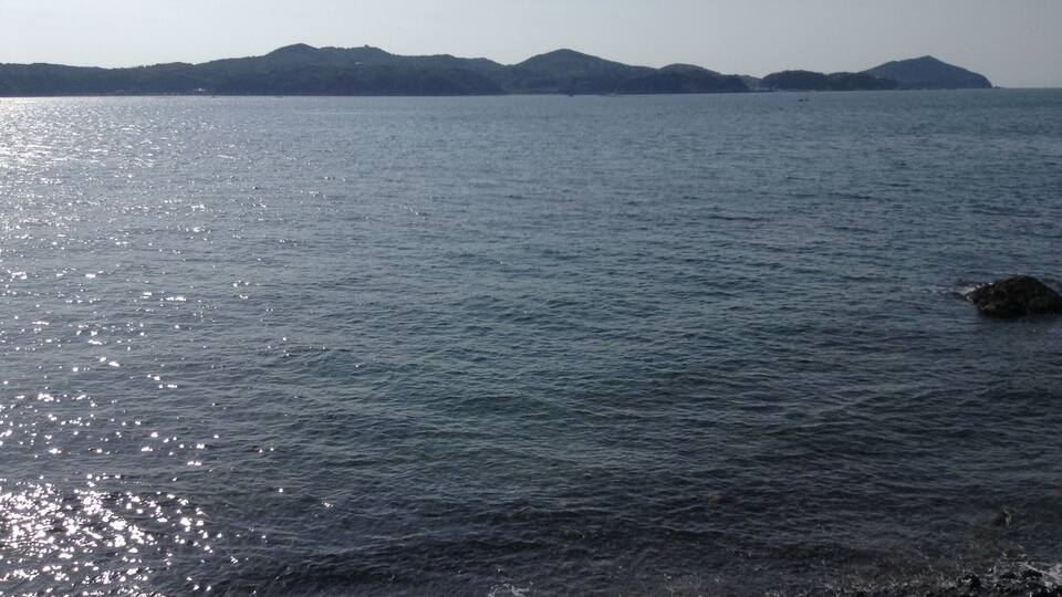 Mar tranquila con costa rocosa y montañas a lo lejos.