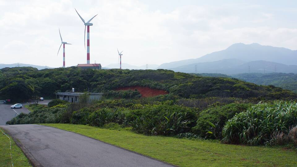 A road with wind turbines in the background and a hilly landscape.