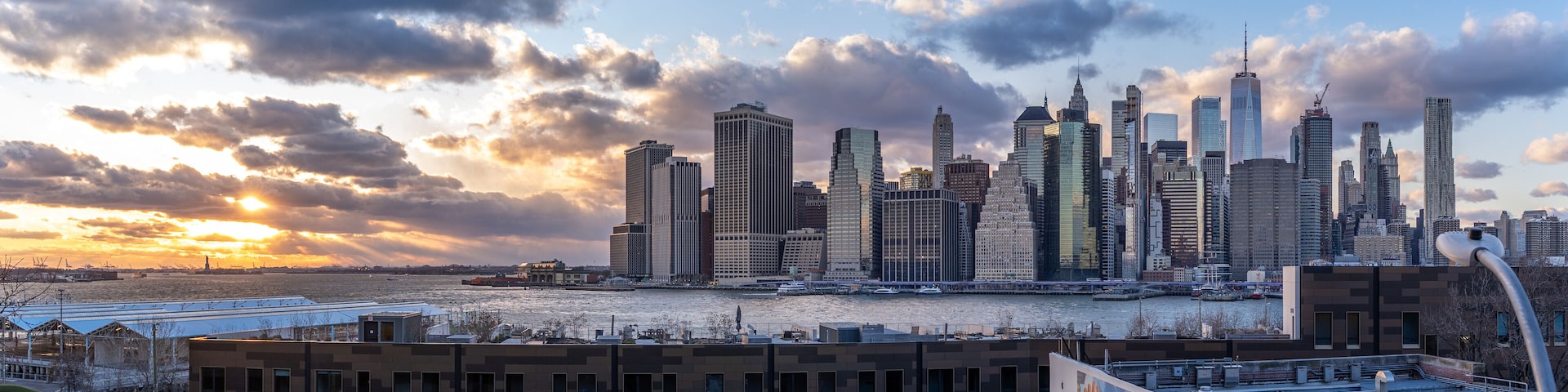Pano wide Panoramic shot of the Manhattan Wall Street Financial district Skyline over the Hudson River, with the statue of lady liberty, shot from a street above brooklyn bridge park