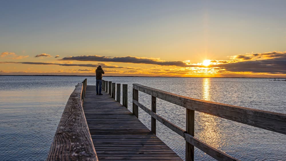 A wooden pier extending into calm water with a sunset in the background.