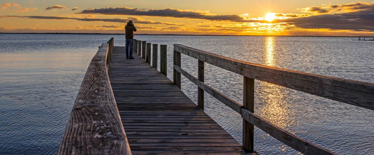 A wooden pier extending into calm water with a sunset in the background.
