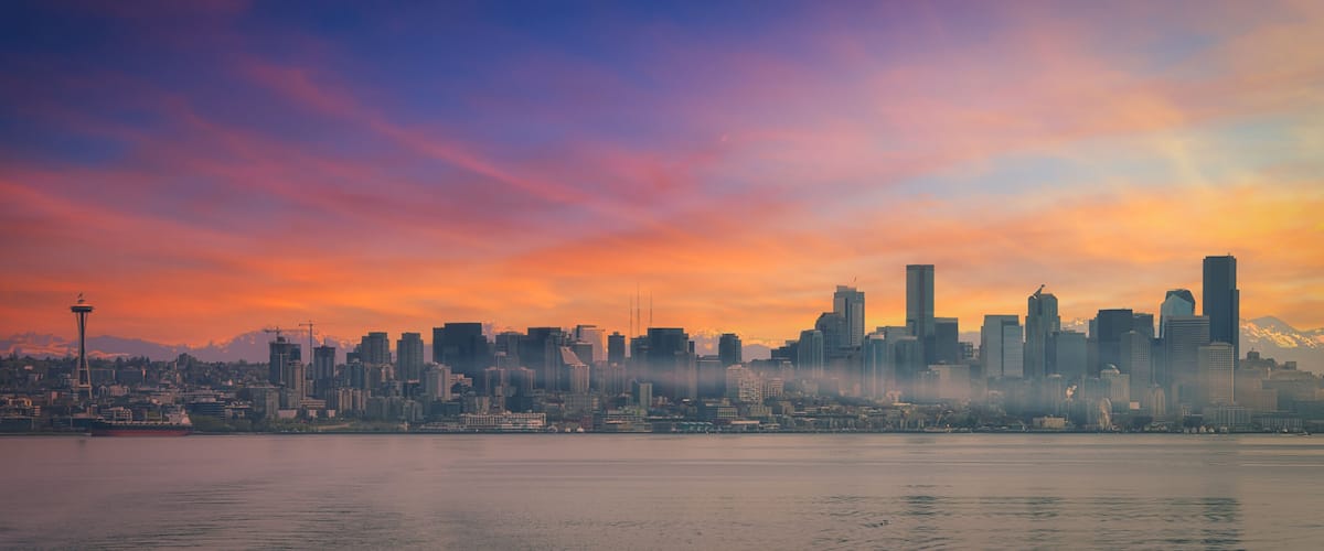 A city skyline at sunset with prominent skyscrapers and the Space Needle.