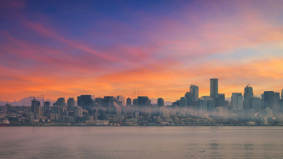 Silhueta urbana ao pôr do sol, com arranha-céus imponentes e a Space Needle.