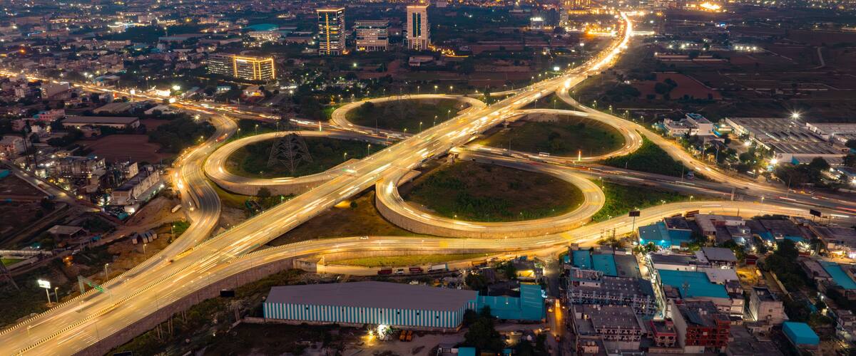 Aerial view of a mesmerizing highway cloverleaf interchange illuminated by golden streetlights under a twilight sky, Golf Course Extension Road, Gurugram, Haryana, India.
