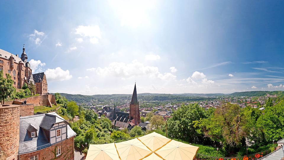 A historic castle, a church, and a scenic view of a town surrounded by hills.