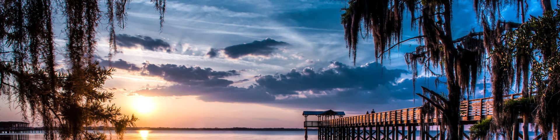 A wooden pier extending into calm waters at sunset with a clear sky.
