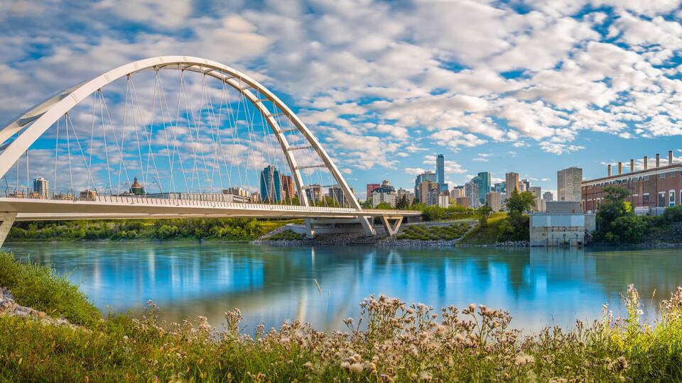A modern bridge over a river with a city skyline in the background.