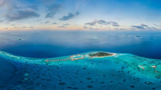 Panoramic aerial view of a luxury resort with boats anchored along the coast on Raa Atoll in the Laccadive Sea, Maldives archipelagos.