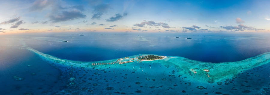 Panoramic aerial view of a luxury resort with boats anchored along the coast on Raa Atoll in the Laccadive Sea, Maldives archipelagos.