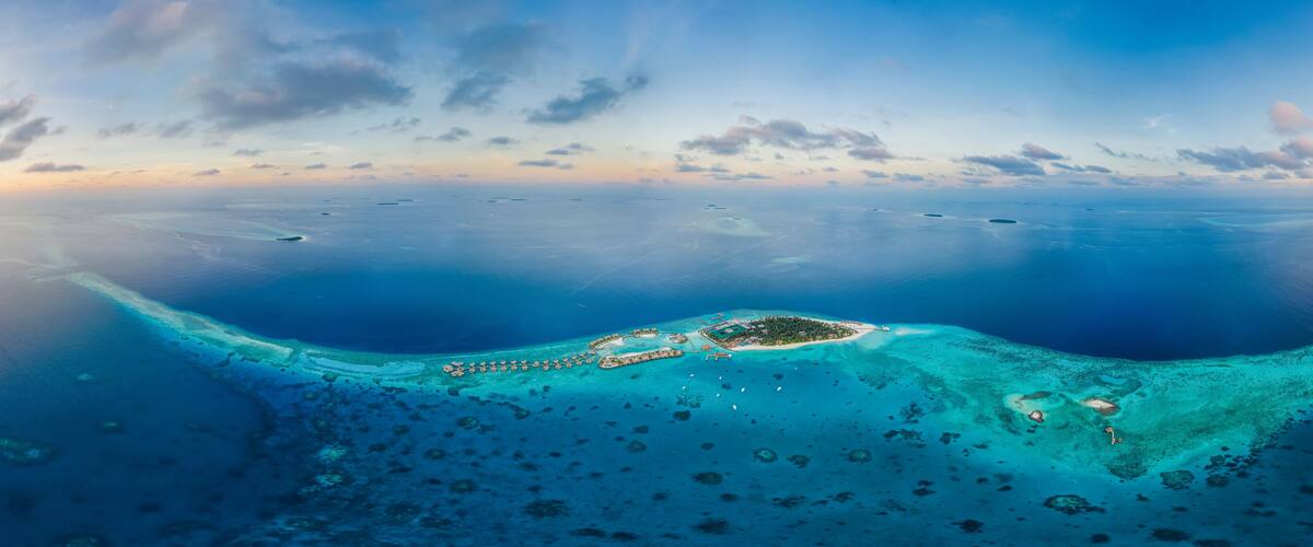An aerial view of a tropical island with clear turquoise waters, a sandy beach, and scattered small islets.