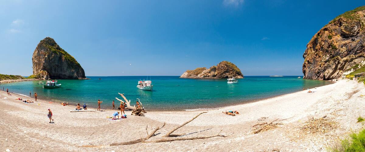 A beach with clear turquoise water, rocky formations, and boats.