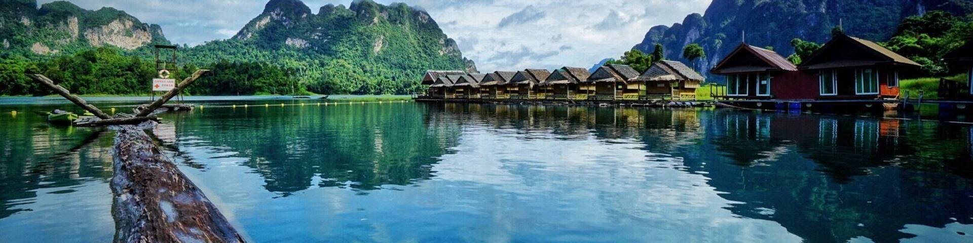 Un lago tranquilo con casas de madera sobre pilotes, rodeado de exuberantes montañas verdes y cielo azul claro.