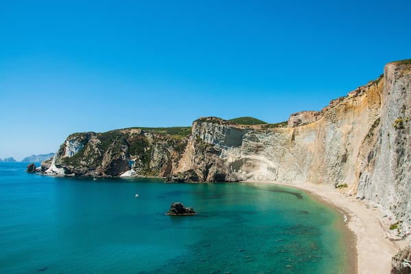 Un paysage côtier caractérisé par des falaises, des eaux turquoise et limpides, et une plage de sable.