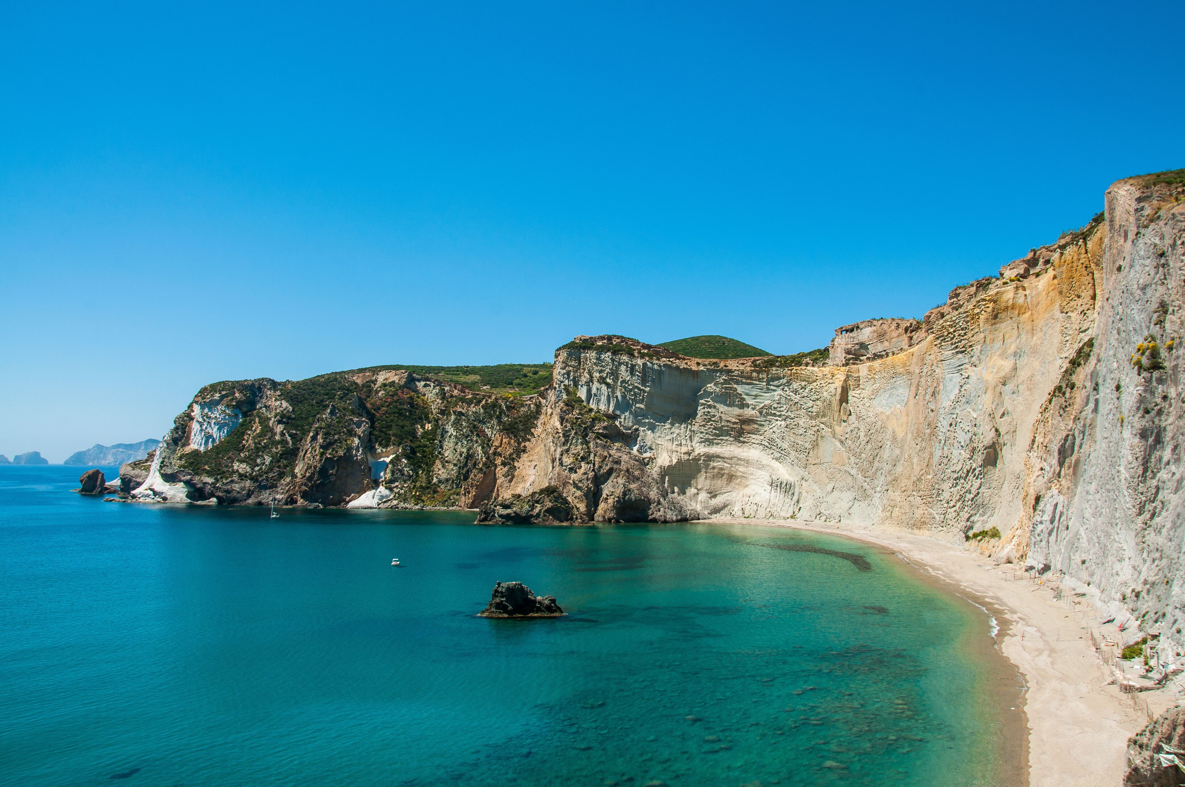 A coastal landscape with cliffs, clear turquoise waters, and a sandy beach.