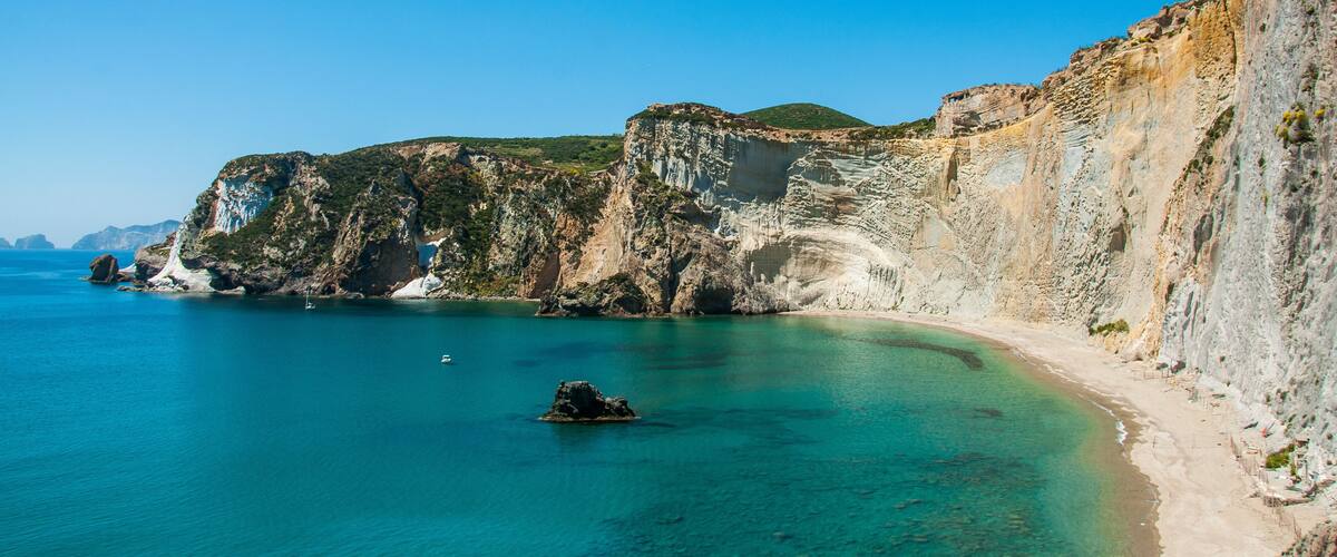 A coastal landscape with cliffs, clear turquoise waters, and a sandy beach.