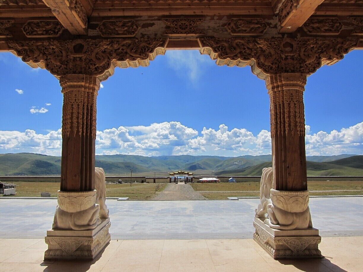A traditional pavilion with ornate columns and a view of a distant landscape with mountains and a clear sky.