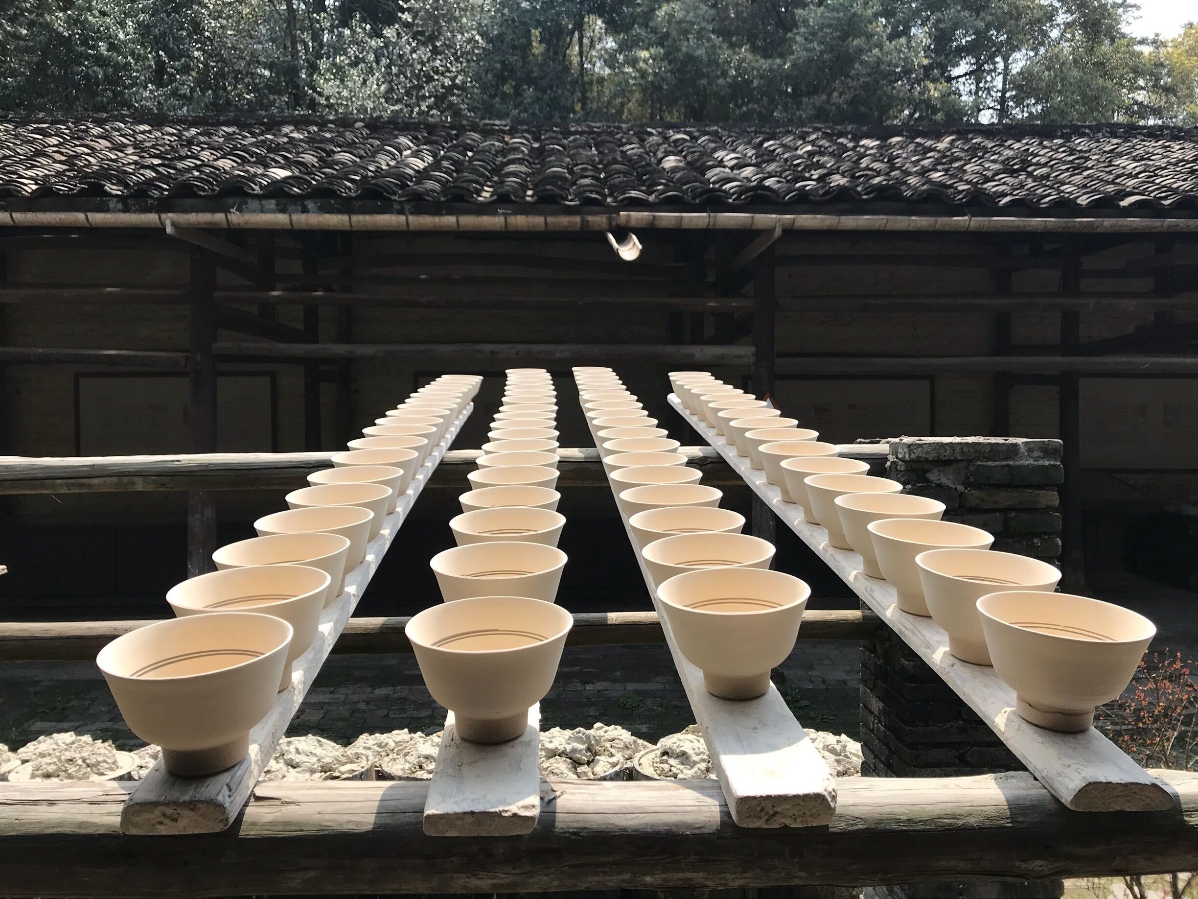 A row of white ceramic bowls on a wooden platform under a tiled roof.