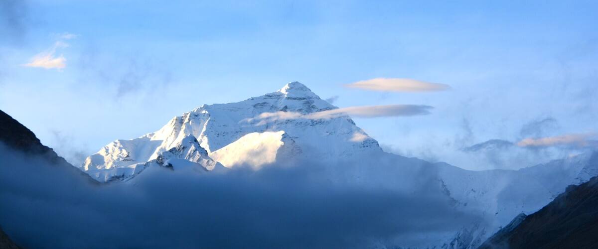 A snow-capped mountain peak with clouds at its base.