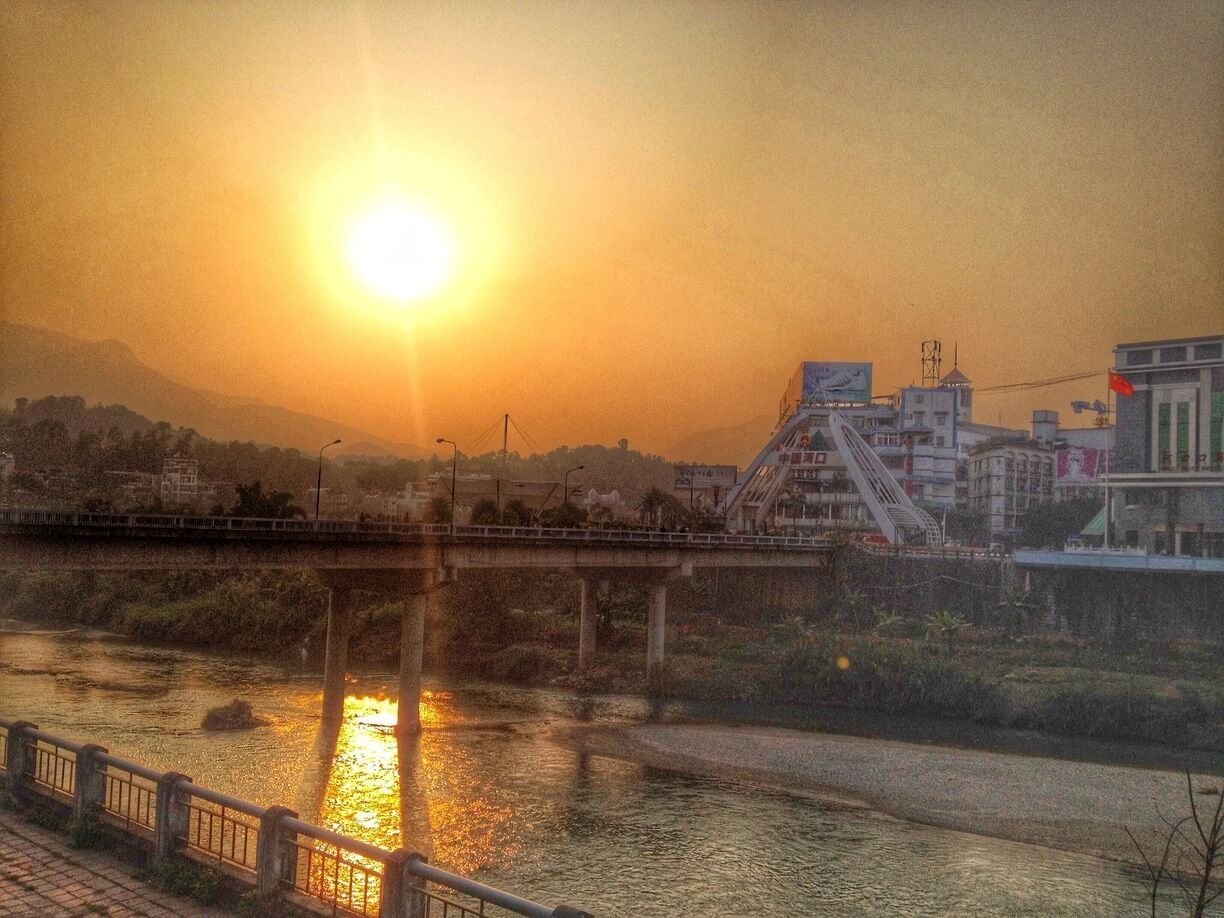 A sunset over a river with a bridge and buildings in the background.