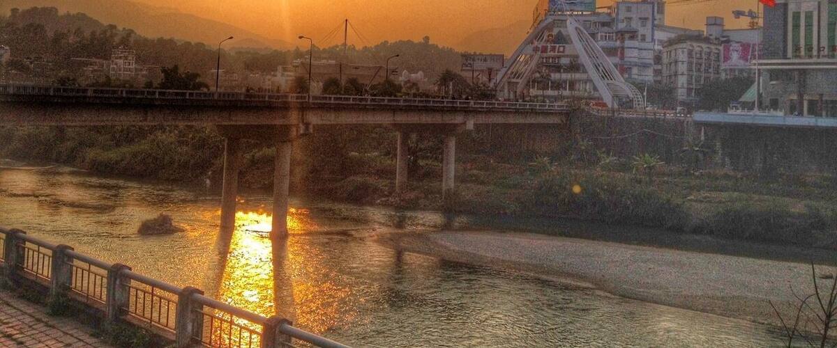 A sunset over a river with a bridge and buildings in the background.