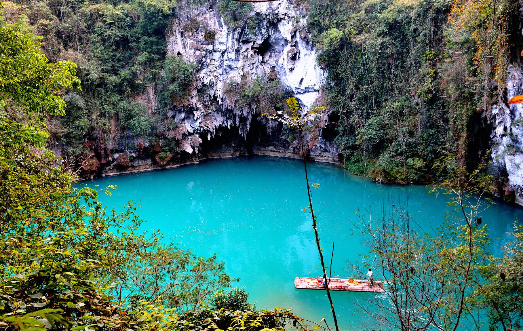 A turquoise lake surrounded by cliffs and dense foliage.