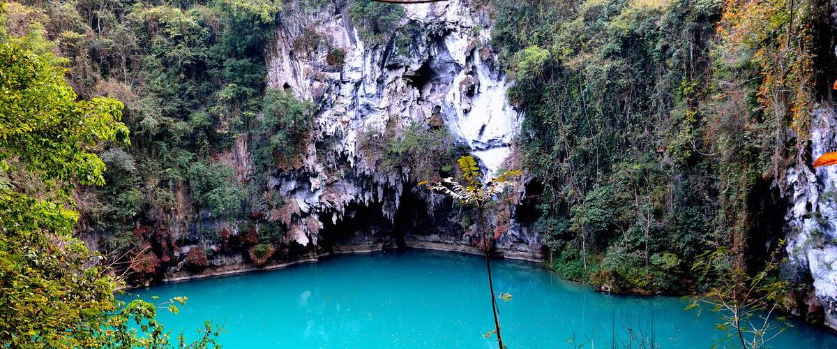 A turquoise lake surrounded by cliffs and dense foliage.