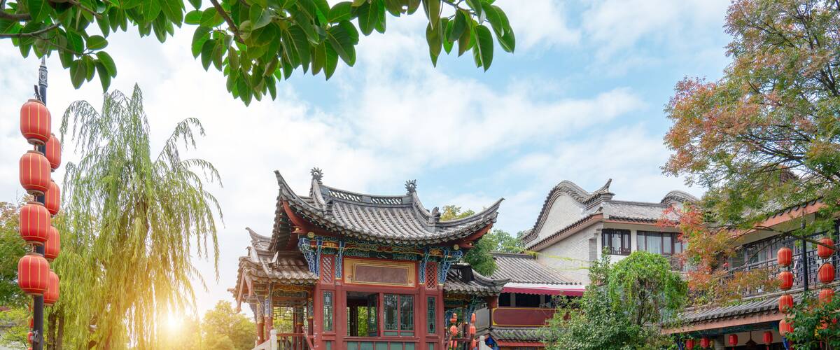 A traditional Chinese pavilion with ornate architecture, a stone bridge, and a pond.