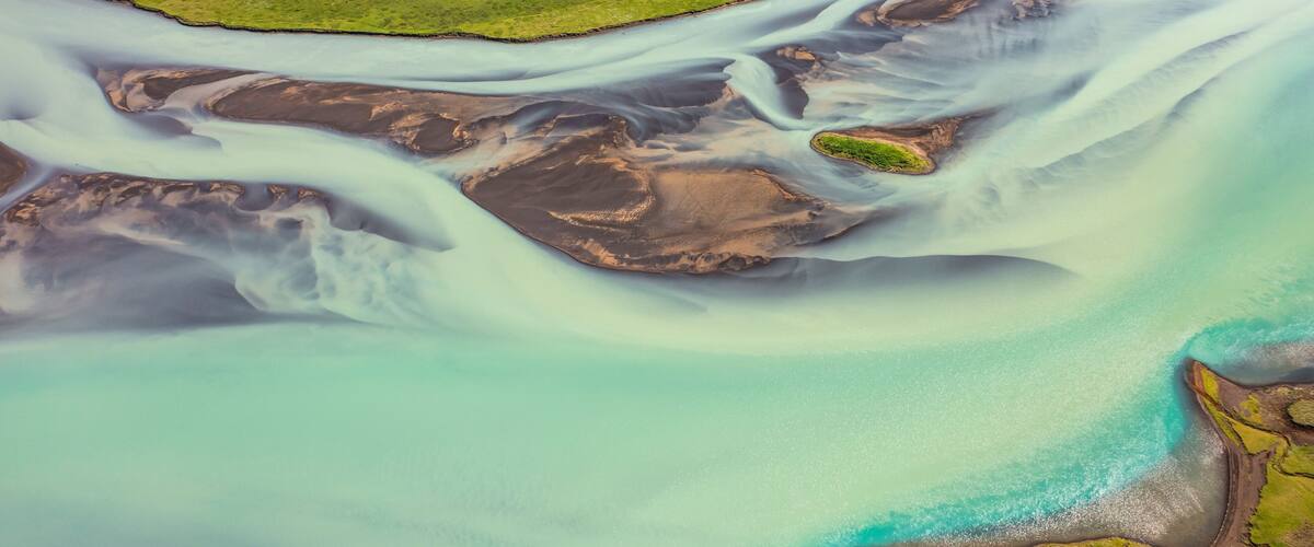 An aerial view of a coastal area with a river flowing into the sea, surrounded by green land and a small island.