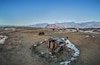 A barren landscape with snow patches, a dilapidated wooden structure, and mountains in the background.
