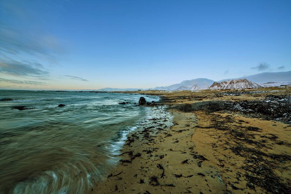 A beach with clear water, sandy shore, and distant mountains.