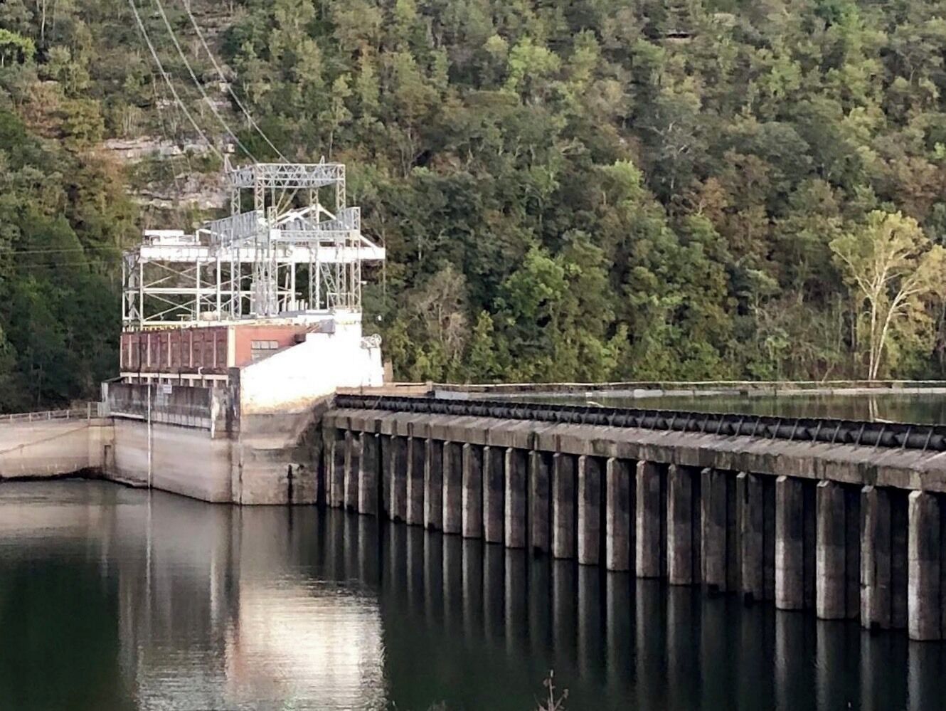 A dam with a water reservoir and a forested hillside in the background.