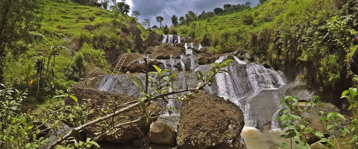 A waterfall cascading over rocks in a lush green valley with a ladder leading up to the top.