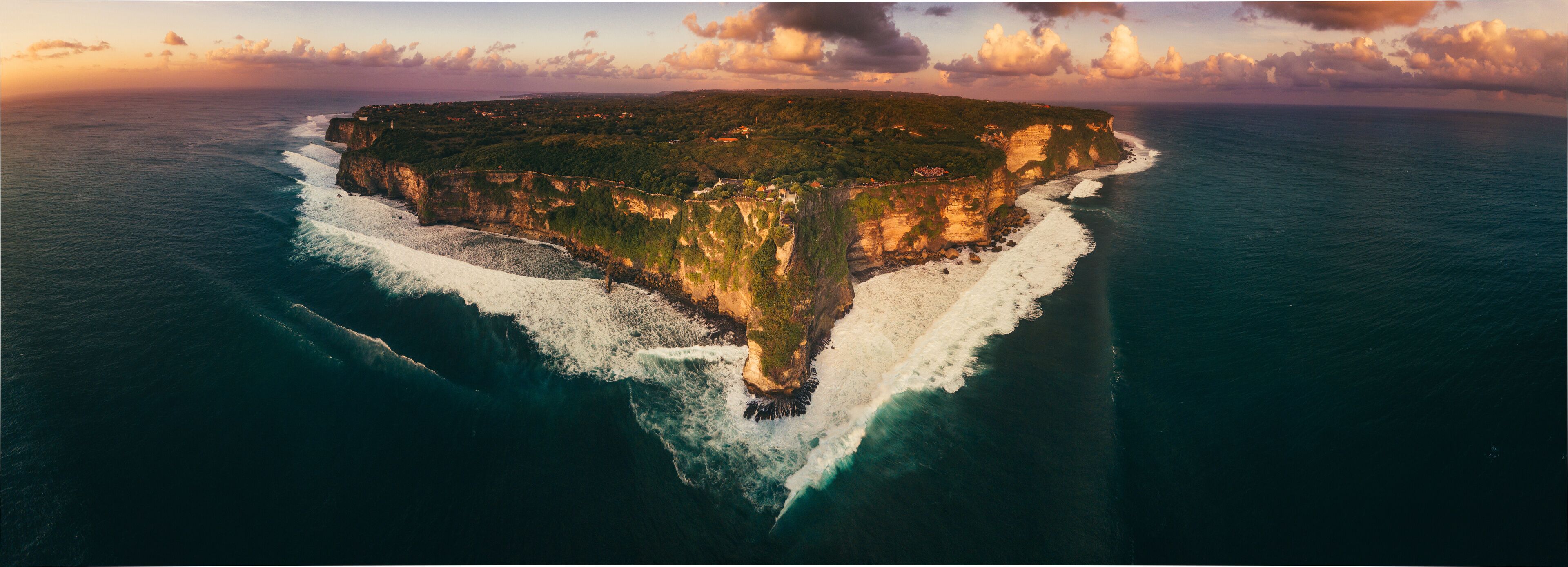 An aerial view of a narrow island with steep cliffs and a small beach.