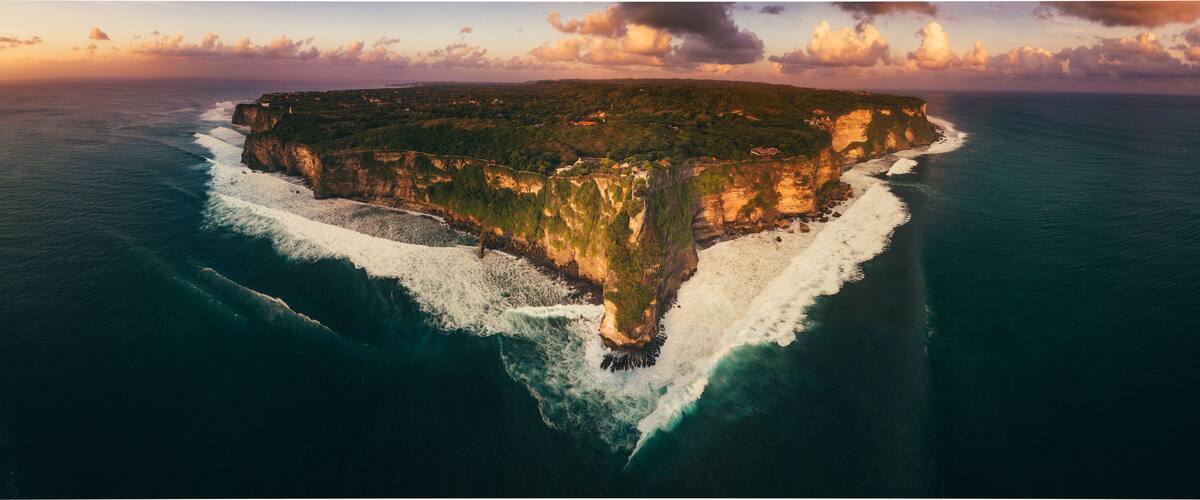 An aerial view of a narrow island with steep cliffs and a small beach.
