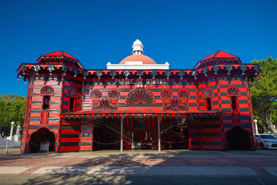 Un edificio colorato con facciata a strisce rosse e nere, una cupola e un cartello con su scritto 'Parque de Bombas'.