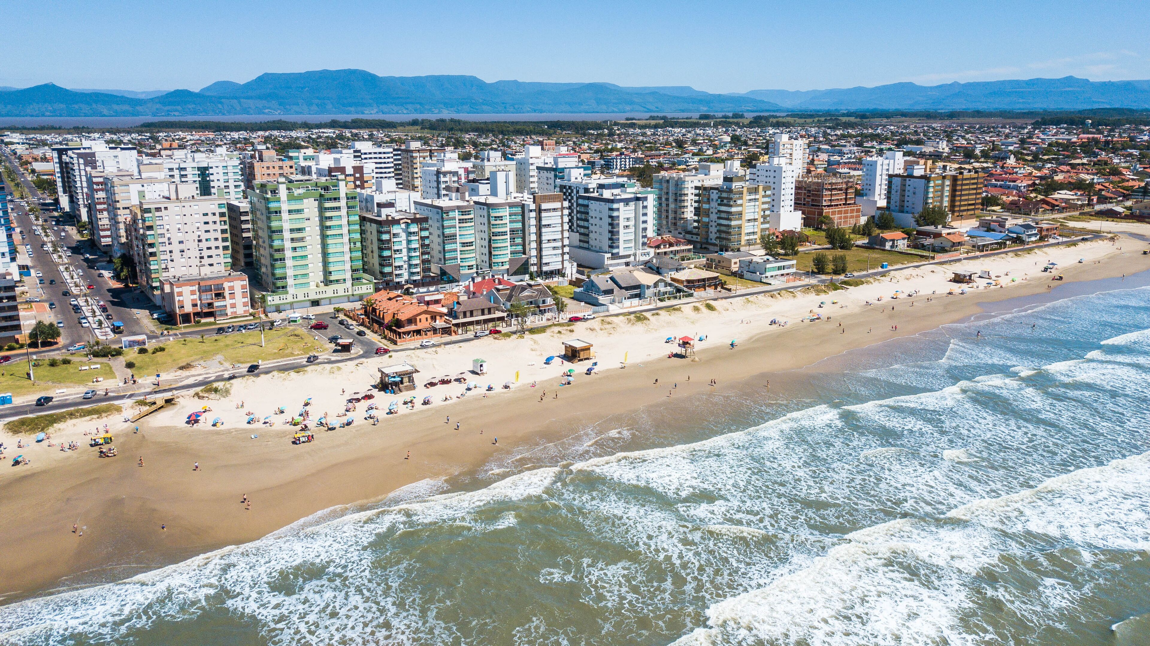 A coastal cityscape with a beach, high-rise buildings, and mountains in the background.