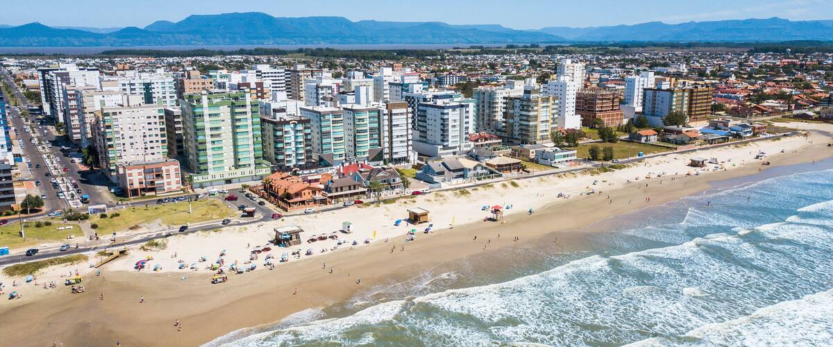 A coastal cityscape with a beach, high-rise buildings, and mountains in the background.