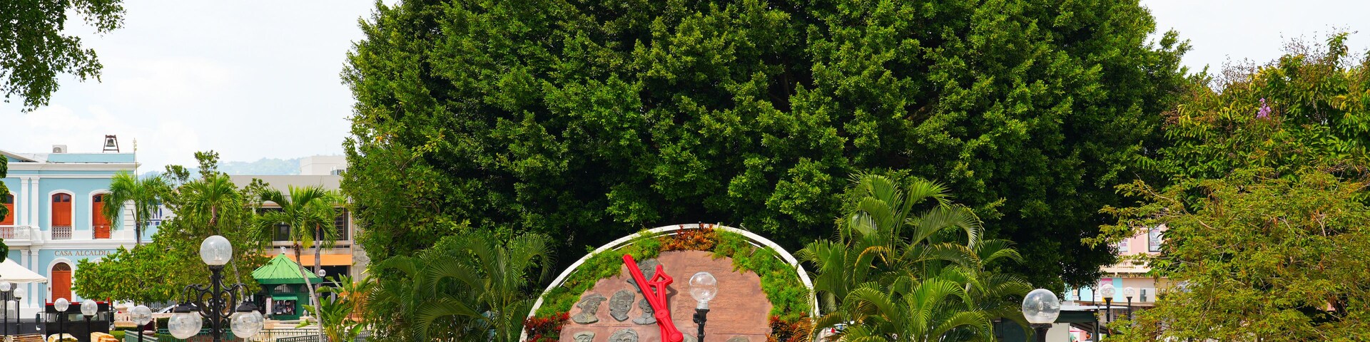 Un gran árbol, un monumento circular y un edificio con fachada azul.