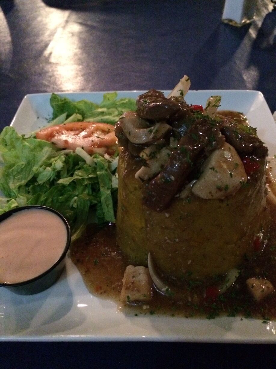 A plate with a meat dish, salad, and a small bowl of sauce.