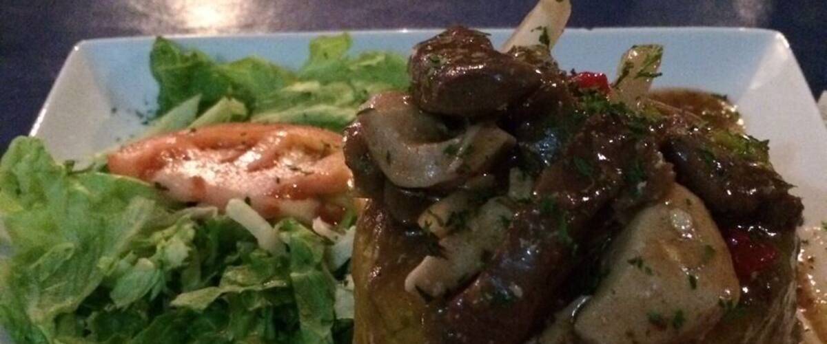 A plate with a meat dish, salad, and a small bowl of sauce.