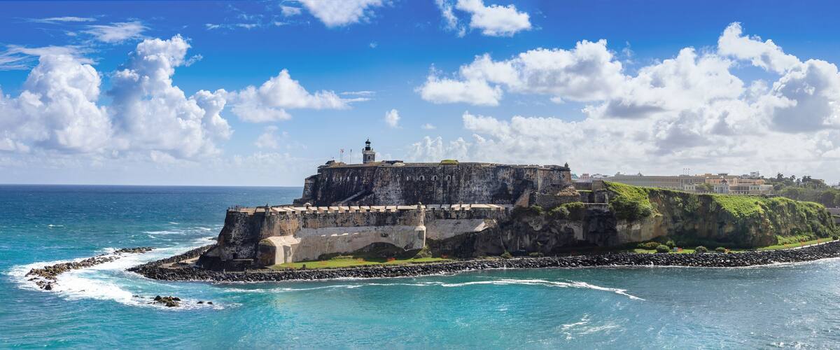 A coastal fortification with a lighthouse, surrounded by turquoise waters and a clear sky.