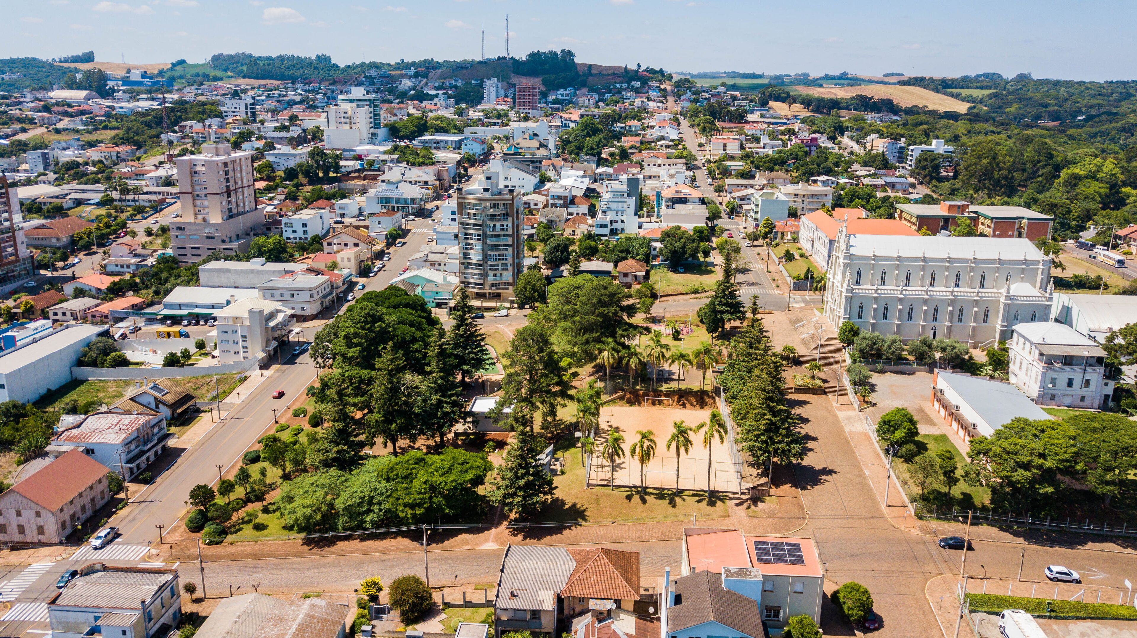 An aerial view of a city with a mix of residential and commercial buildings, a large white building with columns, and a hilly landscape in the background.