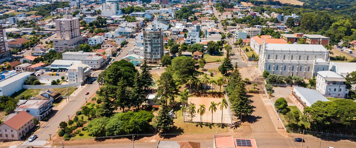 An aerial view of a city with a mix of residential and commercial buildings, a large white building with columns, and a hilly landscape in the background.