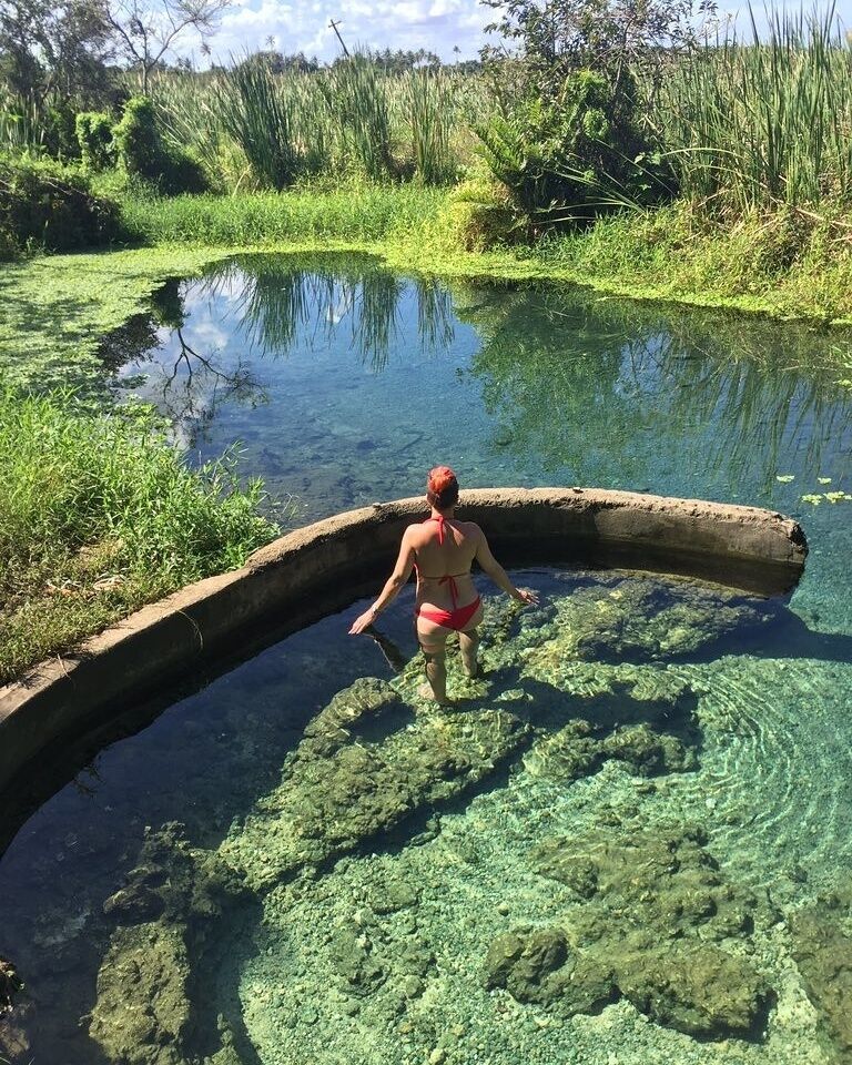 A person in a red swimsuit standing in a clear water body surrounded by greenery.
