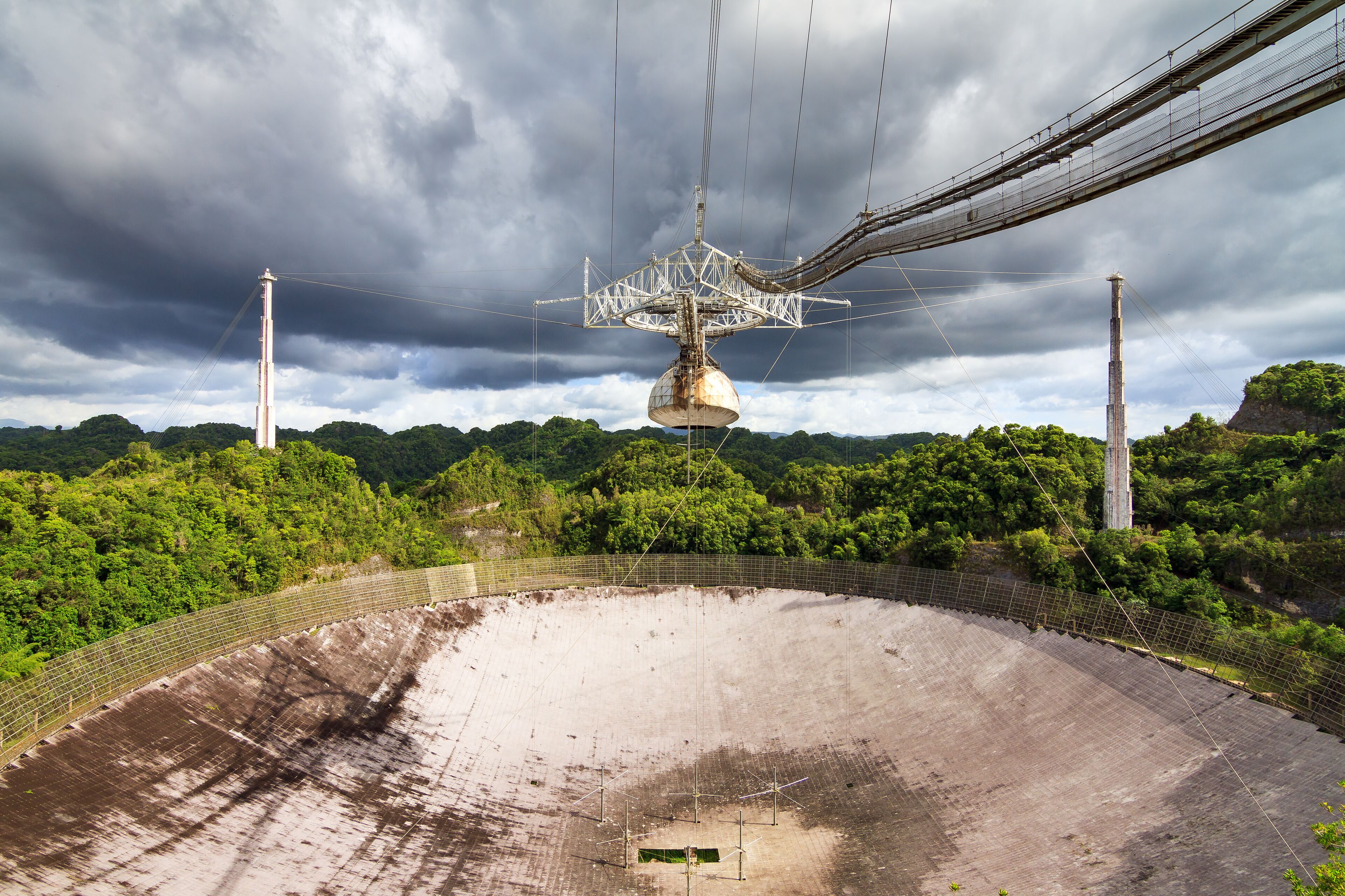 A large, empty dam with a suspension bridge overhead.