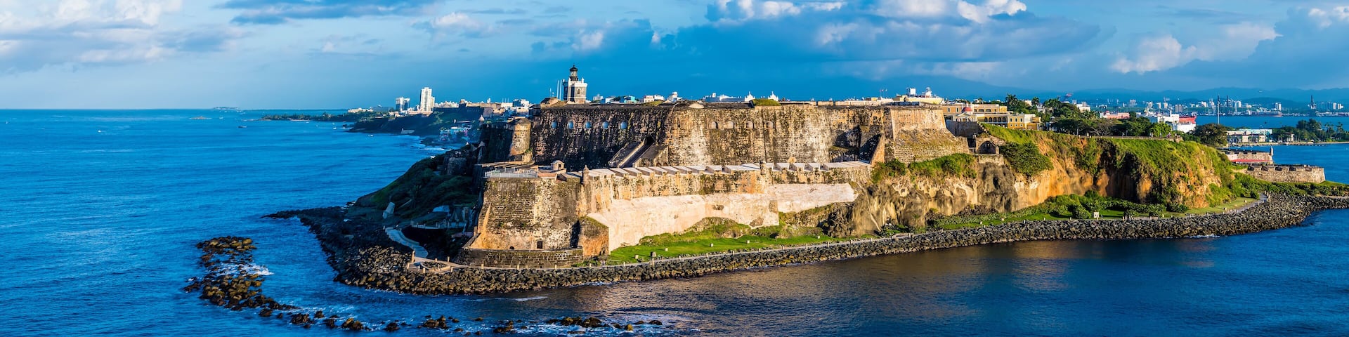 A coastal fortification with a lighthouse, surrounded by water and a cityscape in the background.