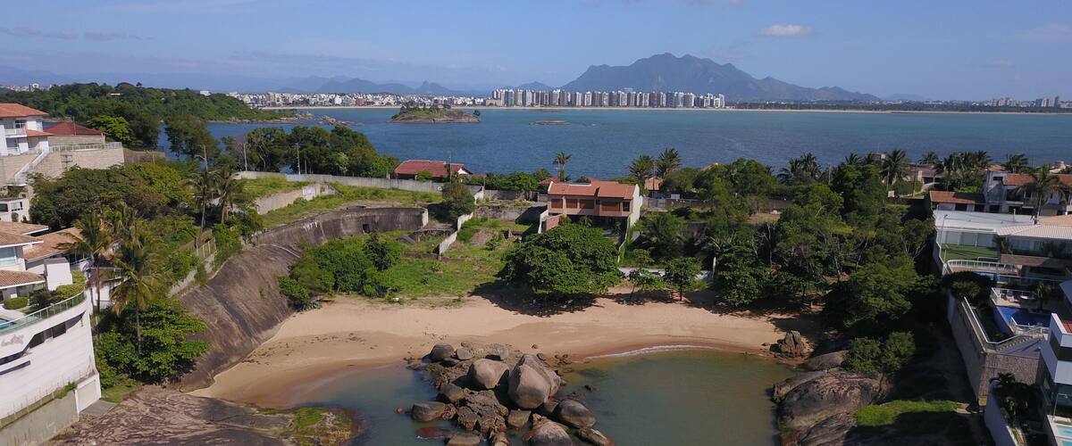 A coastal cityscape with a beach, rocky shoreline, and residential buildings.