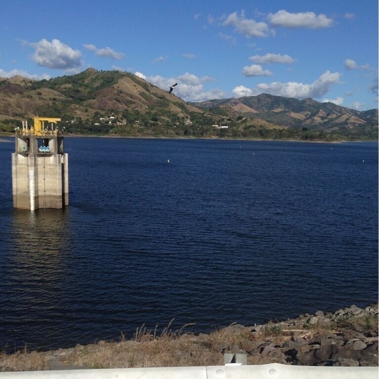 A concrete structure in the water with a yellow roof, surrounded by a calm lake and hills in the background.