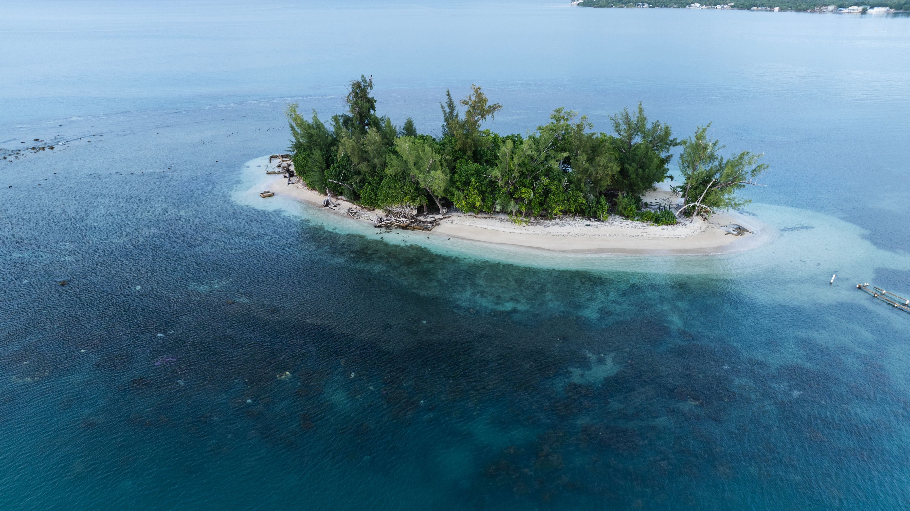 Vista aérea de una pequeña isla con aguas turquesas cristalinas, rodeada por un arrecife de coral.